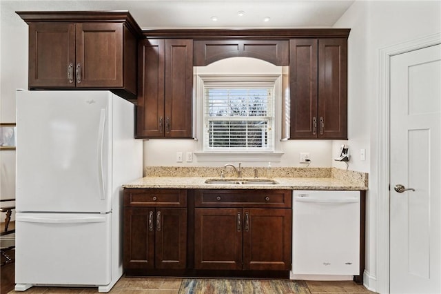 kitchen with a sink, light stone counters, white appliances, and dark brown cabinets