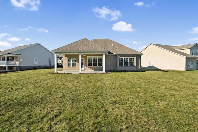 rear view of house with a patio, a lawn, and roof with shingles