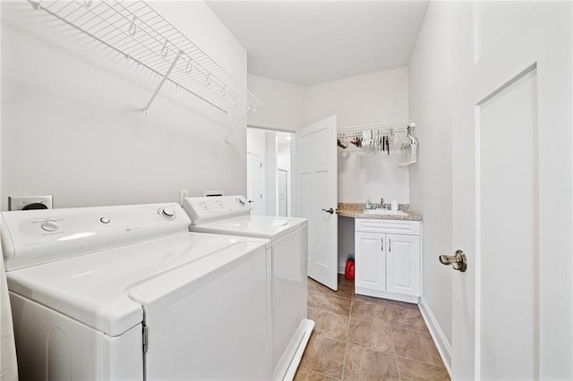 clothes washing area featuring cabinet space, washing machine and dryer, baseboards, and a sink