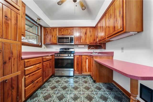 kitchen with ceiling fan, light countertops, brown cabinets, appliances with stainless steel finishes, and a sink