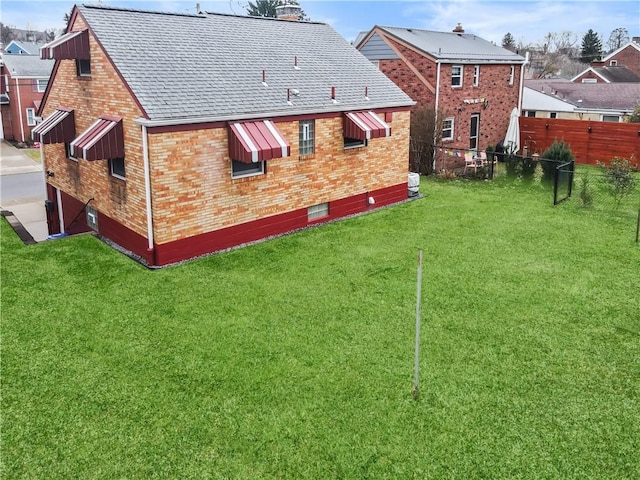 rear view of property with a yard, fence, brick siding, and a shingled roof