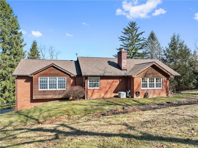 view of front facade with a front yard, brick siding, roof with shingles, and a chimney