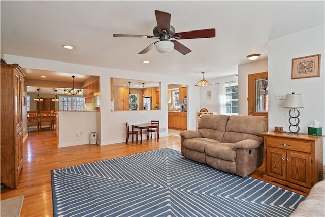 living room with recessed lighting, light wood-style flooring, ceiling fan with notable chandelier, and baseboards