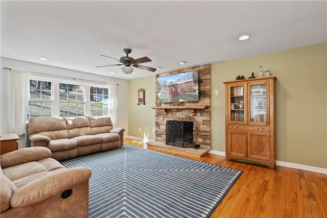 living area with baseboards, recessed lighting, ceiling fan, a stone fireplace, and light wood-style floors