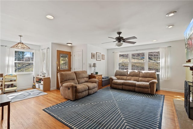 living room featuring recessed lighting, a fireplace with flush hearth, light wood-style floors, and baseboards