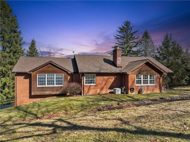 view of front facade with a lawn, brick siding, roof with shingles, and a chimney