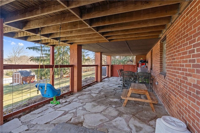 view of patio / terrace featuring a storage unit, an outbuilding, outdoor dining space, and fence