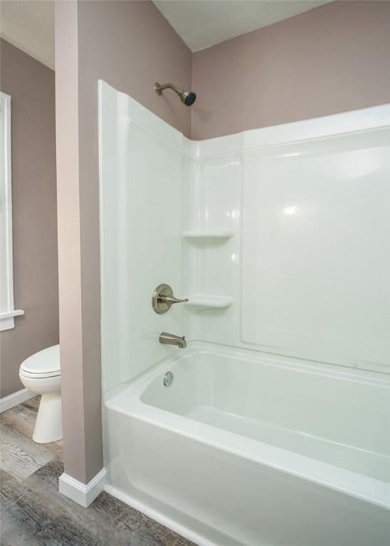 bathroom with toilet, wood finished floors, baseboards, and shower / bathtub combination