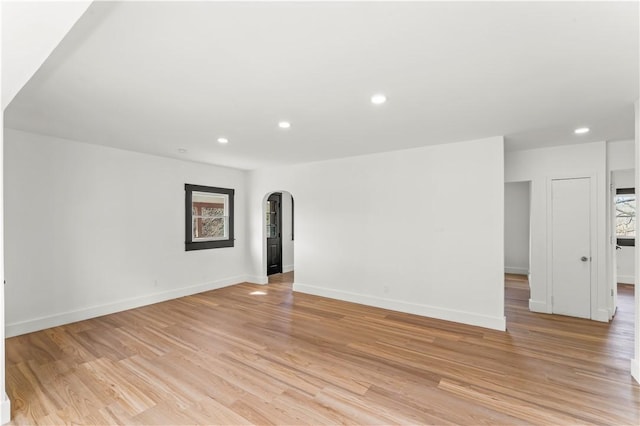 unfurnished room featuring recessed lighting, arched walkways, light wood finished floors, and baseboards