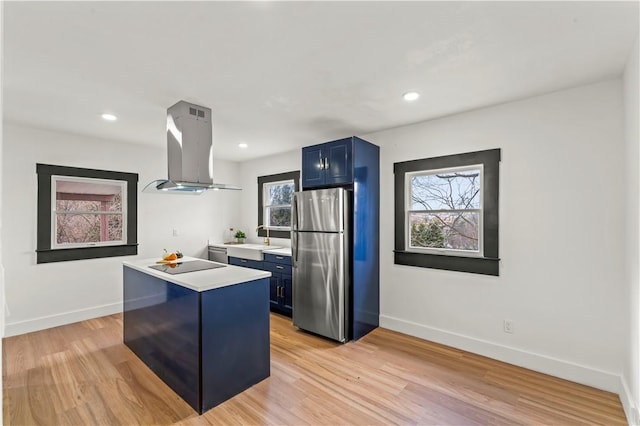 kitchen with blue cabinetry, light countertops, island exhaust hood, freestanding refrigerator, and light wood-style floors