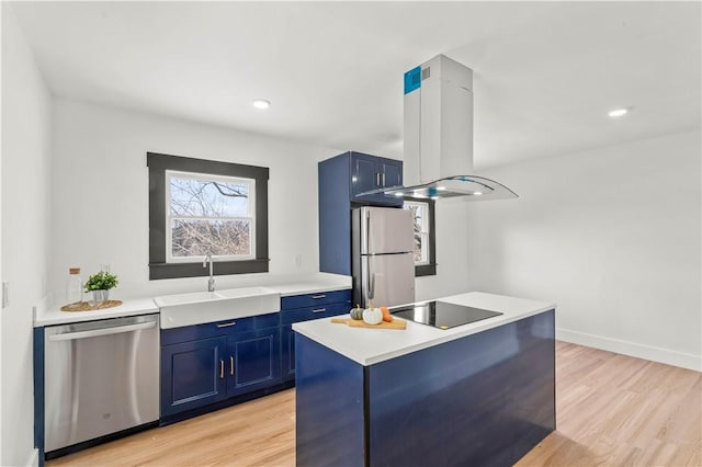 kitchen with blue cabinetry, island exhaust hood, a sink, light wood-style floors, and appliances with stainless steel finishes