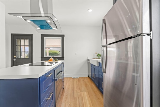 kitchen featuring light wood finished floors, stainless steel appliances, blue cabinets, and light countertops