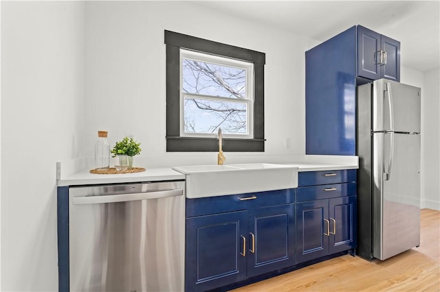 kitchen featuring light countertops, light wood-style flooring, appliances with stainless steel finishes, blue cabinets, and a sink