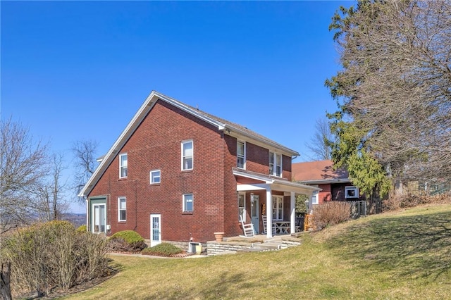 back of property with a yard, brick siding, and covered porch