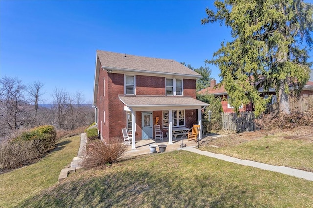 traditional-style home featuring a front lawn, fence, covered porch, and brick siding