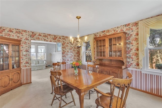 dining space featuring wallpapered walls, a notable chandelier, light colored carpet, and a wainscoted wall