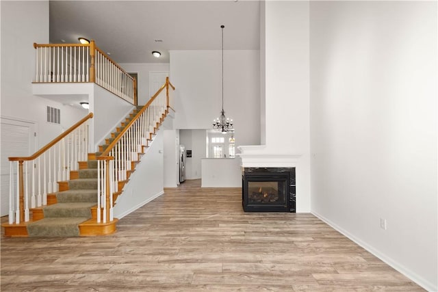 interior space with stairway, wood finished floors, a multi sided fireplace, a towering ceiling, and a notable chandelier