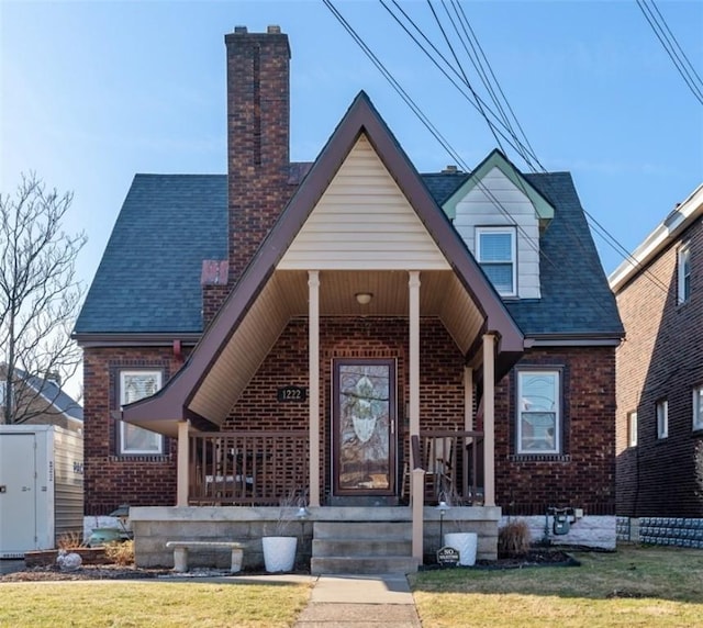 view of front of property with a front lawn, covered porch, brick siding, and a chimney