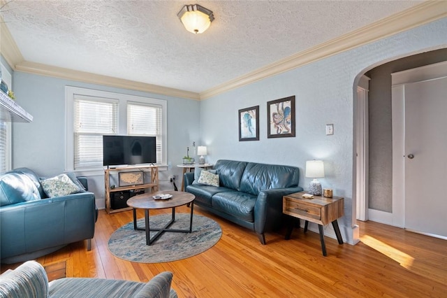 living room with a textured ceiling, crown molding, arched walkways, and light wood-type flooring