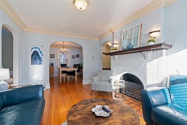 living area featuring a brick fireplace, arched walkways, light wood finished floors, and a textured ceiling