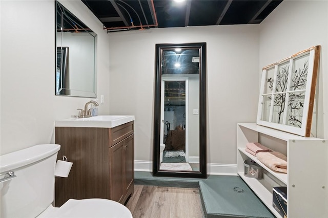 half bath featuring toilet, vanity, baseboards, and wood finished floors