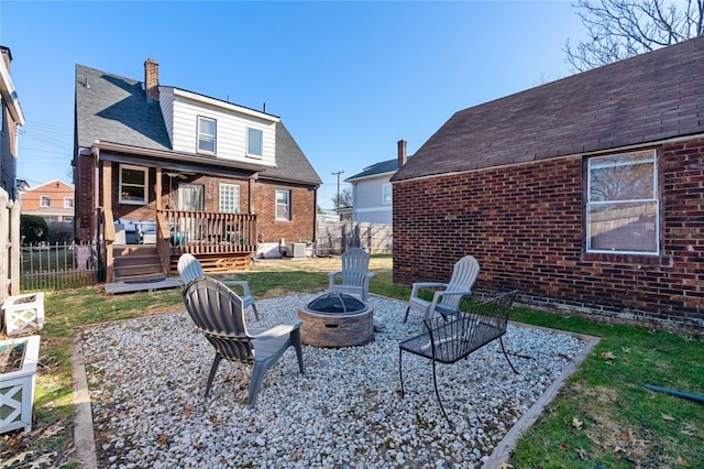 back of property featuring fence, a chimney, a shingled roof, a fire pit, and brick siding