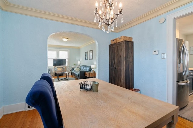 dining room featuring arched walkways, light wood finished floors, a textured wall, and ornamental molding