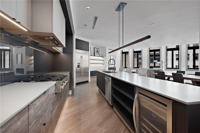 kitchen with modern cabinets, beverage cooler, a sink, appliances with stainless steel finishes, and wall chimney exhaust hood