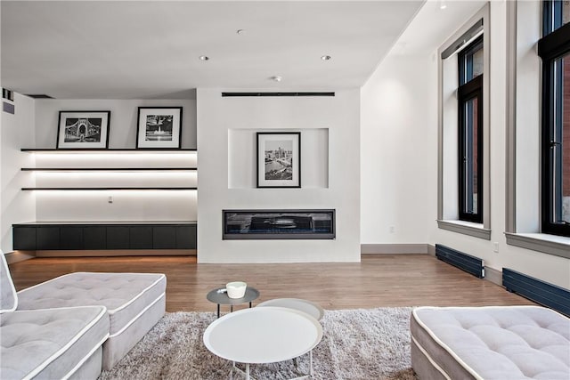 living room featuring a glass covered fireplace, recessed lighting, baseboards, and wood finished floors