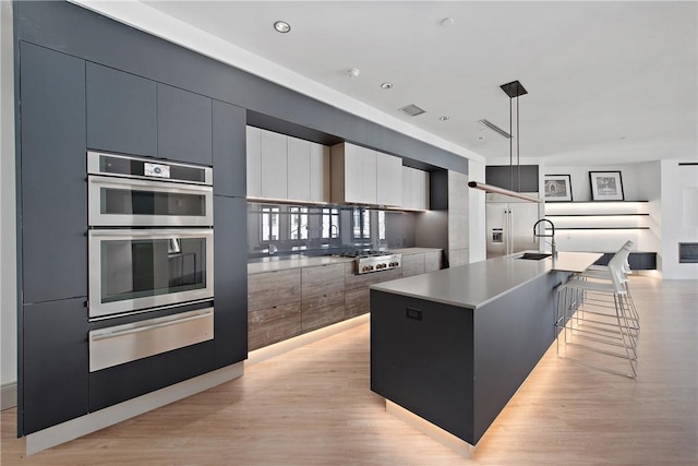 kitchen with a center island with sink, appliances with stainless steel finishes, modern cabinets, a warming drawer, and a sink