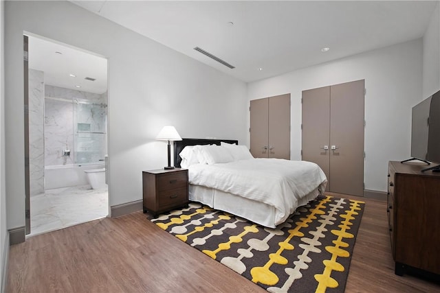 bedroom with visible vents, multiple closets, wood finished floors, and ensuite bathroom