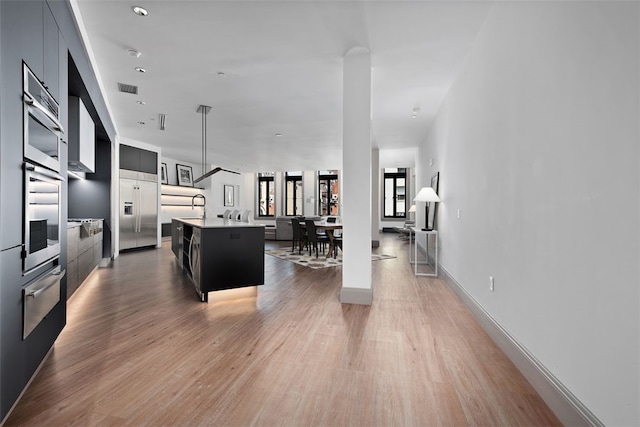 kitchen featuring a warming drawer, visible vents, built in refrigerator, modern cabinets, and a center island with sink