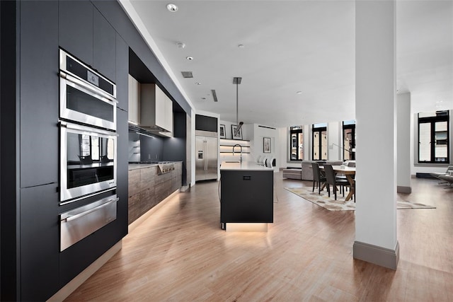 kitchen with a warming drawer, modern cabinets, light wood-style floors, light countertops, and dark cabinets