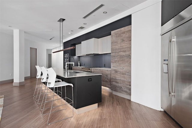 kitchen with visible vents, an island with sink, a sink, modern cabinets, and stainless steel built in refrigerator