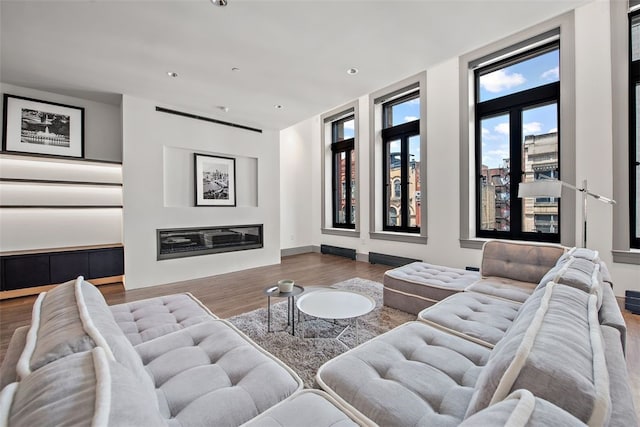 living area featuring a glass covered fireplace, recessed lighting, baseboards, and wood finished floors