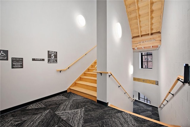 stairway featuring a towering ceiling, baseboards, and carpet floors