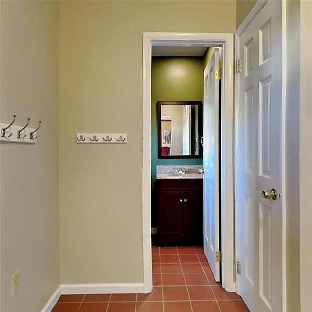 hall with a sink, baseboards, and dark tile patterned floors