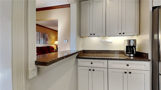 kitchen with freestanding refrigerator, dark stone countertops, white cabinetry, and crown molding