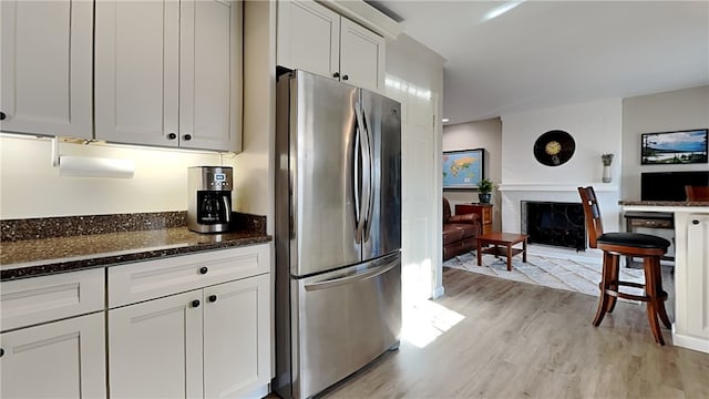 kitchen with dark stone countertops, a fireplace, freestanding refrigerator, white cabinetry, and light wood-type flooring