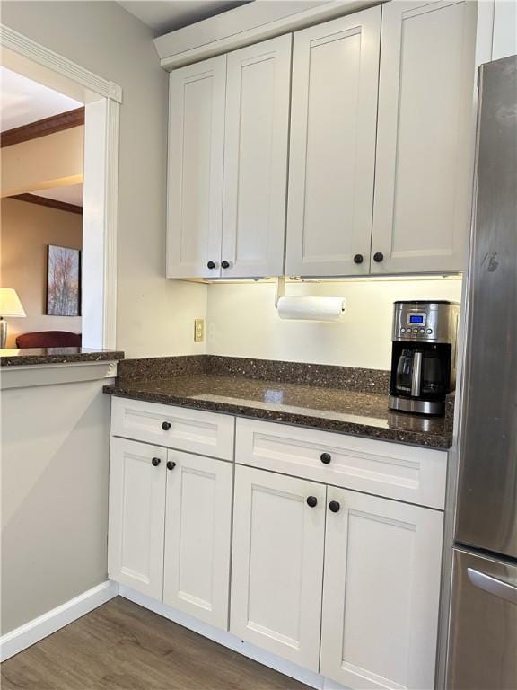 kitchen with dark wood-style floors, baseboards, dark stone counters, freestanding refrigerator, and white cabinetry