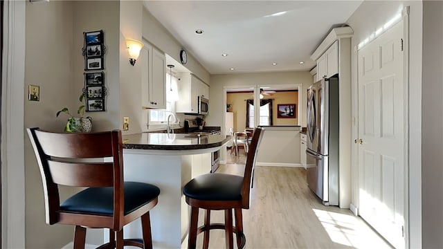 kitchen featuring dark countertops, light wood finished floors, a breakfast bar, appliances with stainless steel finishes, and white cabinets