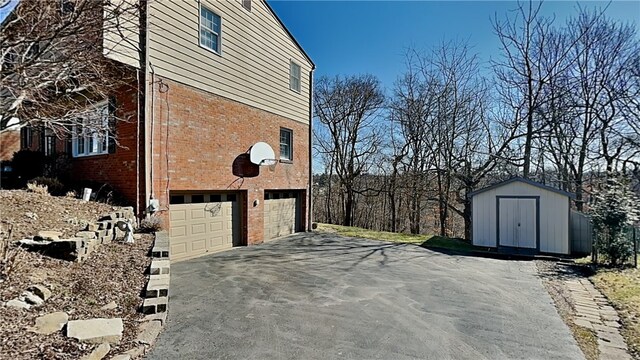 view of property exterior with brick siding, aphalt driveway, an outdoor structure, an attached garage, and a storage unit