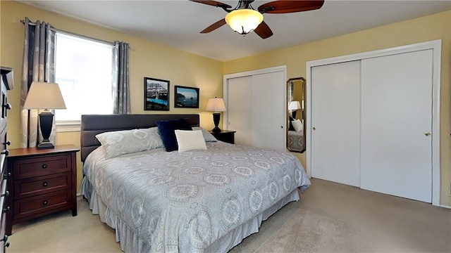 bedroom featuring light colored carpet, two closets, and ceiling fan