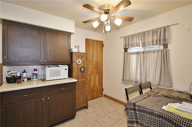 kitchen with white microwave, dark brown cabinets, backsplash, ceiling fan, and light countertops