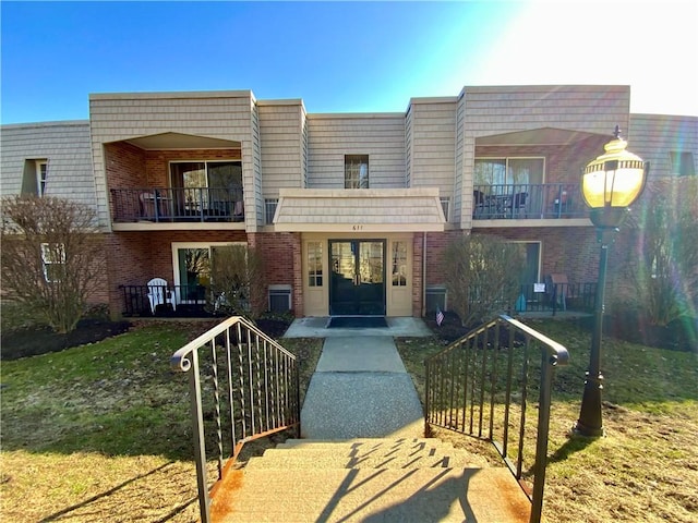 view of front of house featuring mansard roof, brick siding, and a balcony