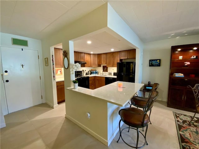 kitchen with visible vents, a breakfast bar, black appliances, light countertops, and brown cabinets