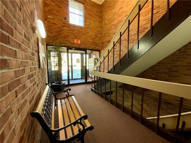 hall with carpet floors, a high ceiling, brick wall, and stairs