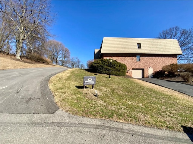 exterior space with aphalt driveway, brick siding, a yard, and an attached garage