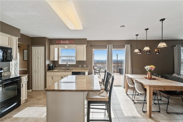 kitchen featuring black appliances, a sink, a kitchen breakfast bar, a kitchen island, and light stone countertops