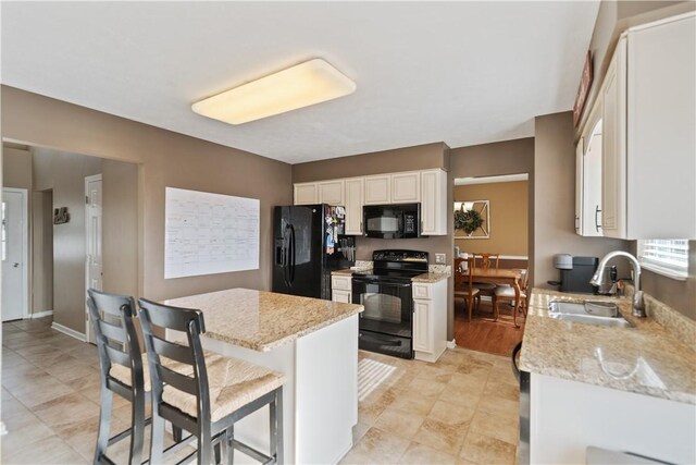 kitchen with a sink, light stone counters, black appliances, and white cabinets